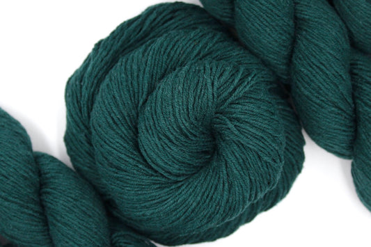 A skein of Dark Forest green, Fingering weight Yarn recycled by hand from unwanted sweaters swirled attractively in the center of the frame. 