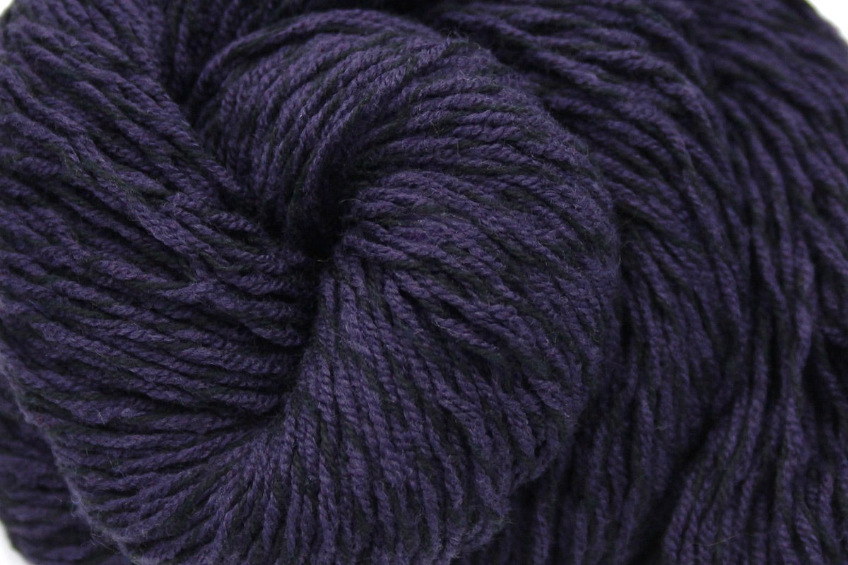 A close up shot of a skein of Dark Purple, Sport weight Yarn recycled by hand from unwanted sweaters beautifully coiled in the center of the frame. 