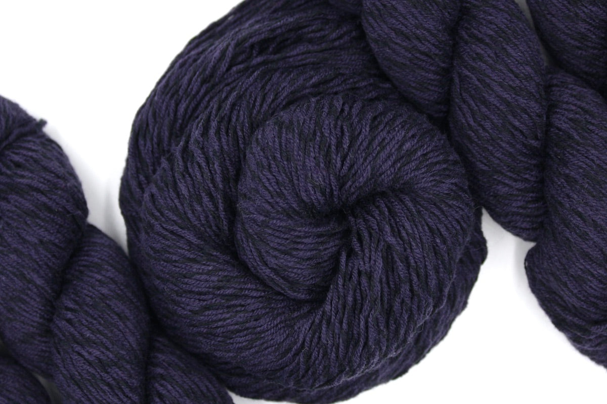 A skein of Dark Purple, Sport weight Yarn recycled by hand from unwanted sweaters swirled attractively in the center of the frame. 
