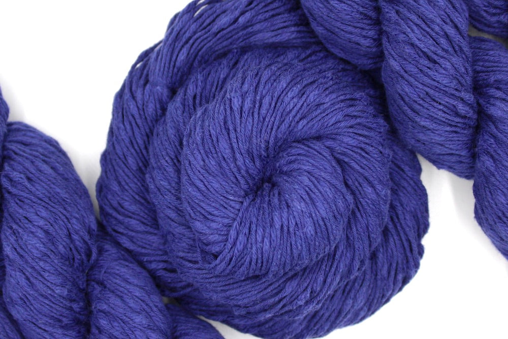 A skein of Deep Violet, Cotton Boucle, Dk weight Yarn recycled by hand from unwanted sweaters swirled attractively in the center of the frame. 