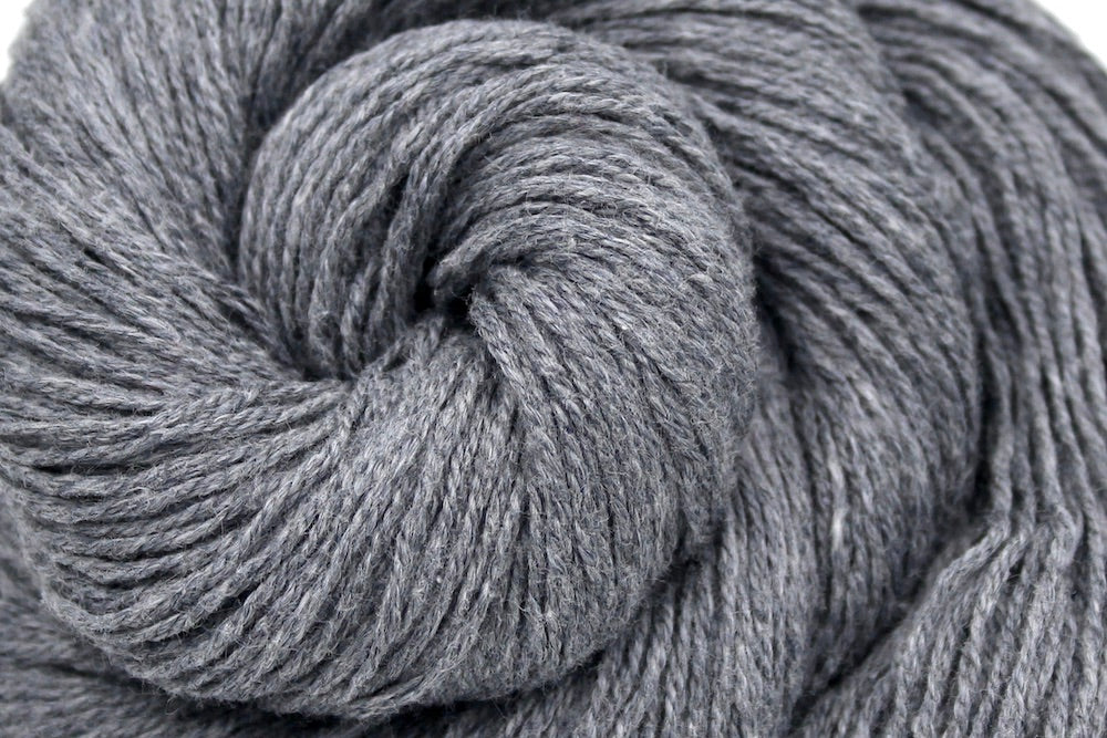 A close up shot of a skein of Light Grey, Cotton Viscose, Fingering weight Yarn recycled by hand from unwanted sweaters beautifully coiled in the center of the frame. 