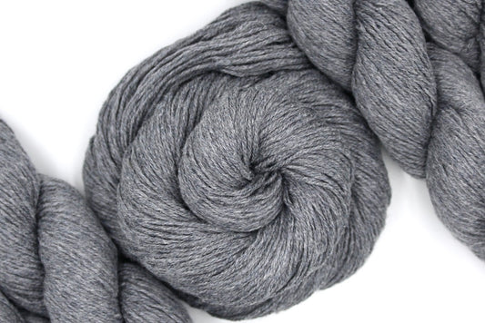A skein of Light Grey, Cotton Viscose, Fingering weight Yarn recycled by hand from unwanted sweaters swirled attractively in the center of the frame. 