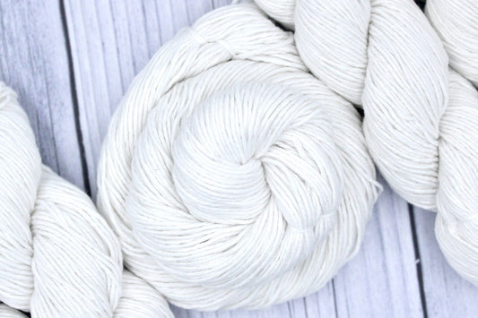 A skein of Pure White, Cotton, Fingering weight Yarn recycled by hand from unwanted sweaters swirled attractively in the center of the frame. 