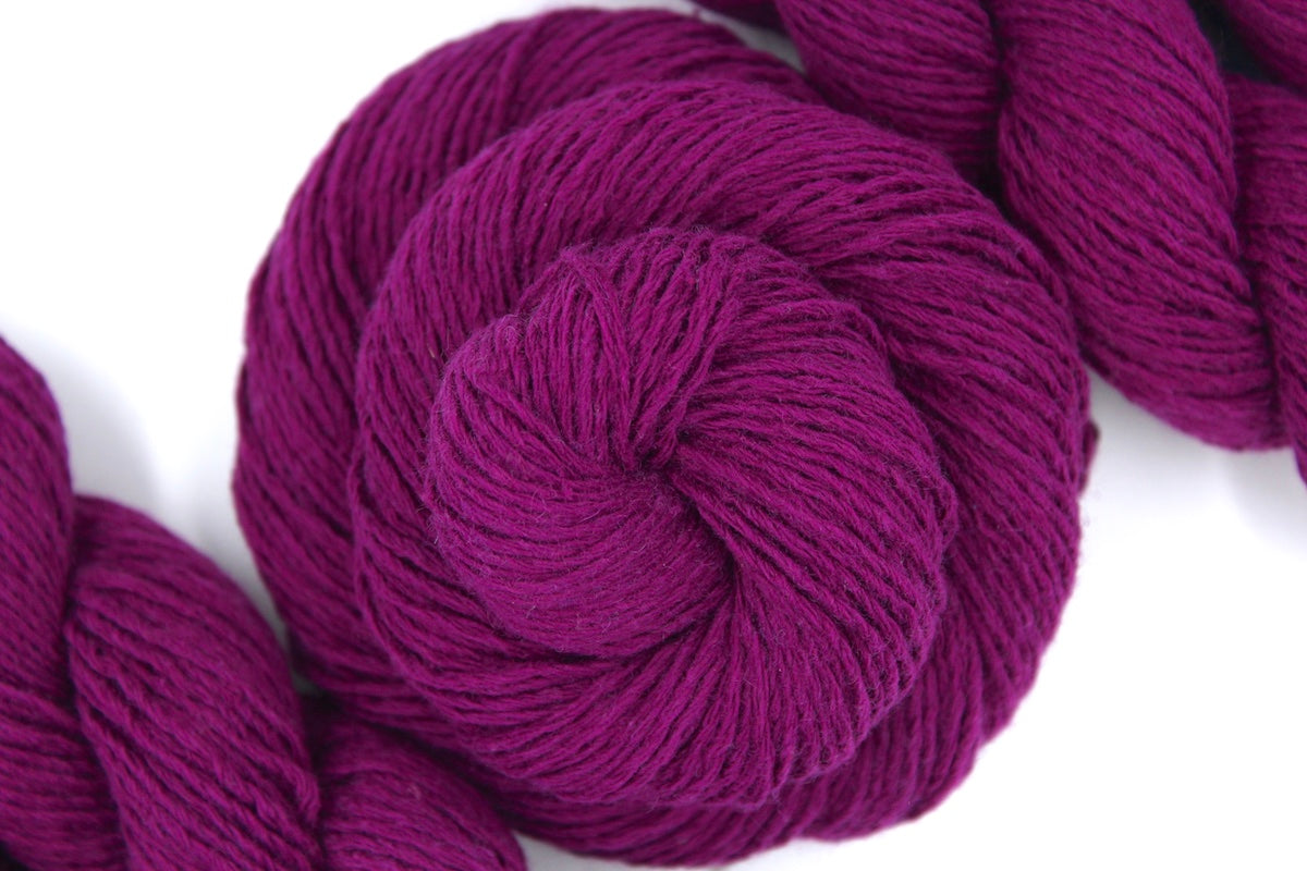 A skein of Magenta, Cotton, Wool, Acrylic, Dk weight Yarn recycled by hand from unwanted sweaters swirled attractively in the center of the frame. 
