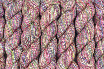 Six one of a kind, Dk Weight, hand dyed variegated skeins of multicolored Pink, Green, Yellow, Blue, and Purple self-striping Hand spun Yarn, made of Hand Dyed Wool and Sparkly Nylon Fiber, lined up side by side. 