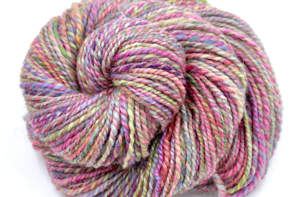 A close up view of a one of a kind, Dk Weight, hand dyed variegated skein of multicolored Pink, Green, Yellow, Blue, and Purple self-striping Hand spun Yarn, made of Hand Dyed Wool and Sparkly Nylon Fiber. 