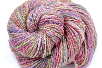A close up view of a one of a kind, Dk Weight, hand dyed variegated skein of multicolored Pink, Green, Yellow, Blue, and Purple self-striping Hand spun Yarn, made of Hand Dyed Wool and Sparkly Nylon Fiber. 