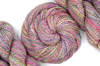 A one of a kind Dk Weight, hand dyed variegated skein of multicolored Pink, Green, Yellow, Blue, and Purple self-striping Hand spun Yarn, made of Hand Dyed Wool and Sparkly Nylon Fiber; coiled attractively in the center of the frame. 