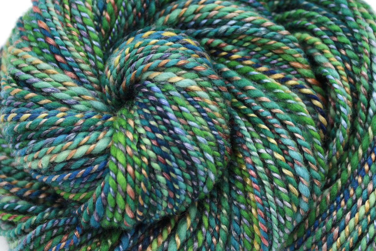 A close up view of a one of a kind, hand dyed variegated skein of multicolored Green, Blue, Gold, and Red self-striping wool Yarn. 