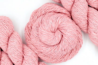 A skein of Vegan, Pink, 60% Cotton, 40% Acrylic, Dk Weight Yarn recycled by hand from unwanted sweaters swirled attractively in the center of the frame. 