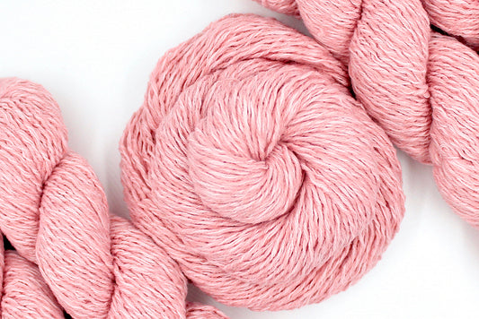 A skein of Vegan, Pink, 60% Cotton, 40% Acrylic, Dk Weight Yarn recycled by hand from unwanted sweaters swirled attractively in the center of the frame. 