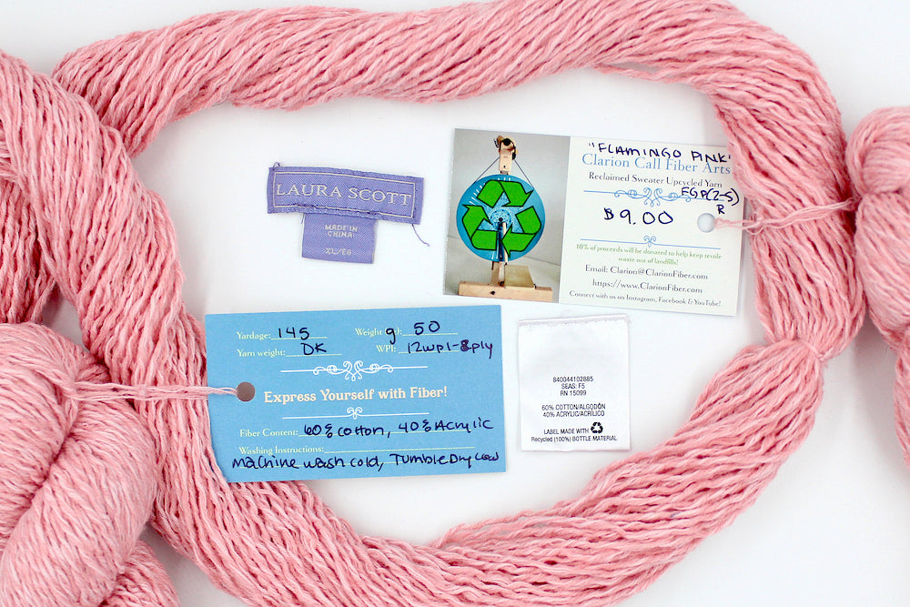 A skein of Vegan, Pink, 60% Cotton, 40% Acrylic, Dk Weight yarn encircling the sweater labels it was recycled from, as well as the hand written yarn tags detailing the specs of this recycled yarn to help you make your next project! 
