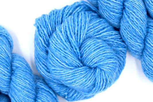 A skein of Light Baby Blue, Acrylic, Nylon, Wool, Cashmere, Dk weight Yarn recycled by hand from unwanted sweaters swirled attractively in the center of the frame. 