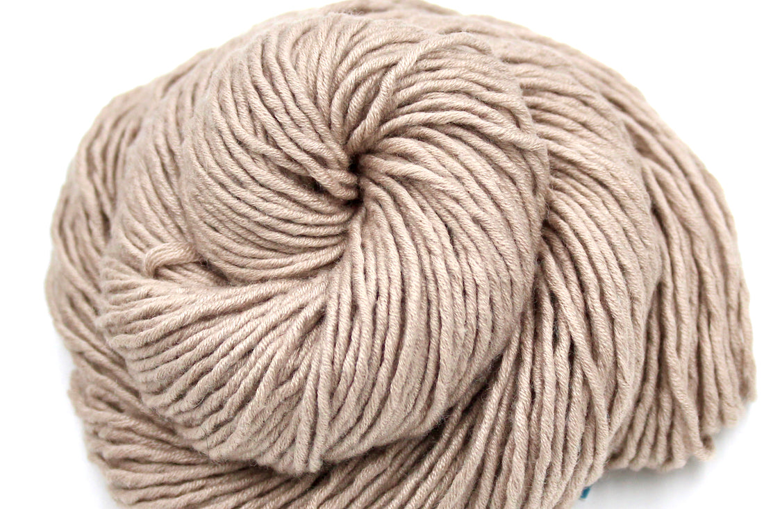 A close up shot of a skein of beige, 40% Wool, 30% Nylon, 30% Modal, Worsted Weight Yarn recycled by hand from unwanted sweaters beautifully coiled in the center of the frame. 