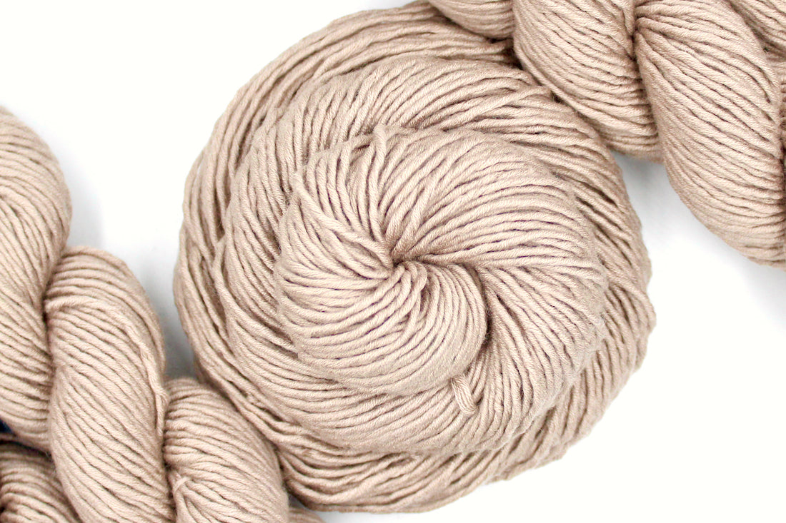 A skein of Tan, 40% Wool, 30% Nylon, 30% Modal, Worsted Weight Yarn recycled by hand from unwanted sweaters swirled attractively in the center of the frame. 