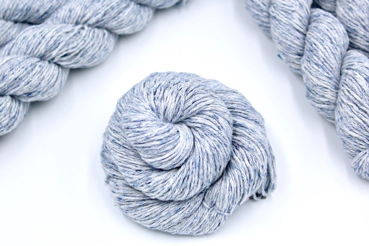 A skein of Pale Blue Speckled, Cotton/ Acrylic, Dk weight Yarn recycled by hand from unwanted sweaters swirled attractively in the center of the frame. 