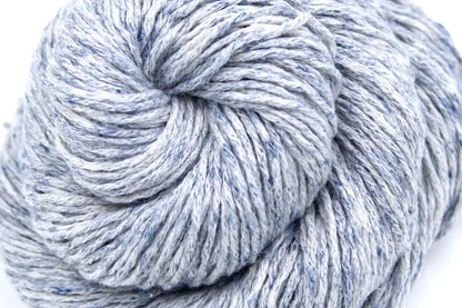 A close up shot of a skein of Pale Blue Speckled, Cotton/ Acrylic, Dk weight Yarn recycled by hand from unwanted sweaters beautifully coiled in the center of the frame. 