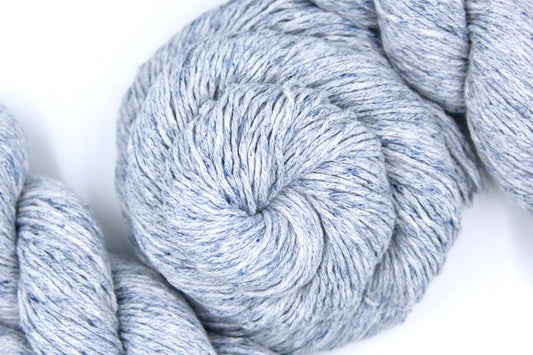 A skein of Pale Blue Speckled, Cotton/ Acrylic, Dk weight Yarn recycled by hand from unwanted sweaters swirled attractively in the center of the frame. 
