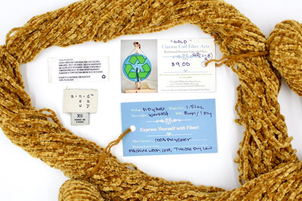 A skein of Yellow Gold, Chenille Polyester, Worsted Weight yarn encircling the sweater labels it was recycled from, as well as the hand written yarn tags detailing the specs of this upcycled yarn to help you make your next project! 