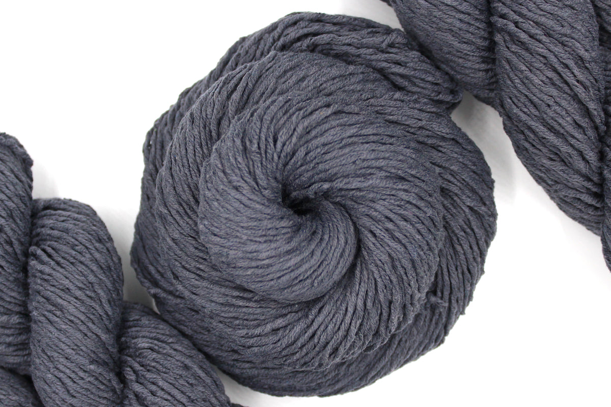 A skein of Vegan, Dark Grey, 60% Cotton, 40% Acrylic, Worsted Weight Yarn recycled by hand from unwanted sweaters swirled attractively in the center of the frame. 