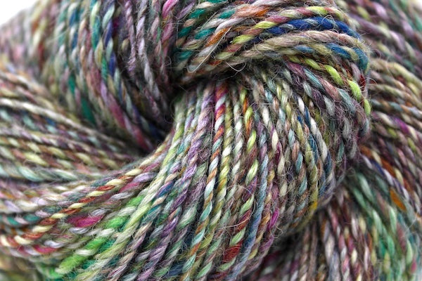 A close up view of a one of a kind, hand dyed variegated skein of multicolored Navy, Maroon, Fuchsia, Teal, Kelly Green, Lime Green, and Gold self-striping wool Yarn. 