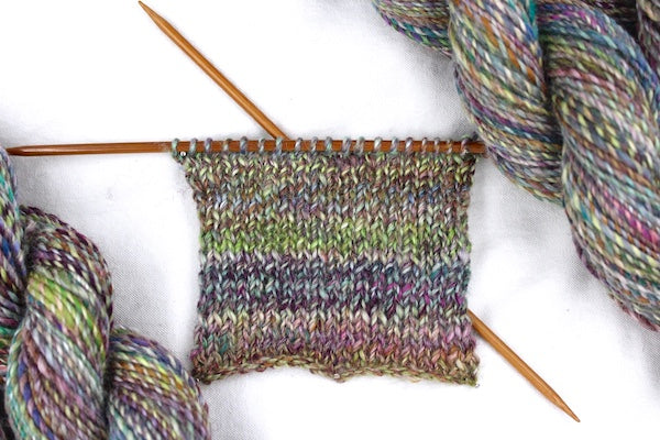 A sample swatch knitted from a one of a kind, hand dyed variegated skein of multicolored Navy, Maroon, Fuchsia, Teal, Kelly Green, Lime Green, and Gold self-striping wool Yarn. 