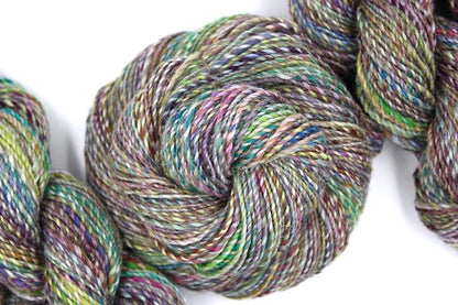 A one of a kind, hand dyed variegated skein of multicolored Navy, Maroon, Fuchsia, Teal, Kelly Green, Lime Green, and Gold self-striping wool Yarn coiled attractively in the center of the frame. 