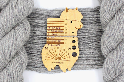 A skein of Light heathered grey, 90% Lambs wool and 10% cashmere, Dk Weight Yarn recycled by hand from unwanted sweaters draped over the center of the frame with one strand on top of a Llama shaped Yarn weight tool, to better illustrate the thickness of the yarn. 