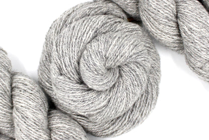 A skein of Light heathered grey, 90% Lambs wool and 10% cashmere, Dk Weight Yarn recycled by hand from unwanted sweaters swirled attractively in the center of the frame. 