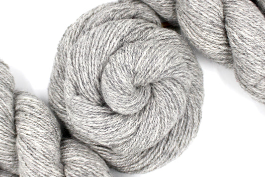 A skein of Light heathered grey, 90% Lambs wool and 10% cashmere, Dk Weight Yarn recycled by hand from unwanted sweaters swirled attractively in the center of the frame. 