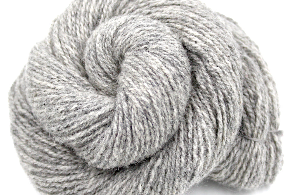 A close up shot of a skein of Light heathered grey, 90% Lambs wool and 10% cashmere, Dk Weight Yarn recycled by hand from unwanted sweaters beautifully coiled in the center of the frame. 