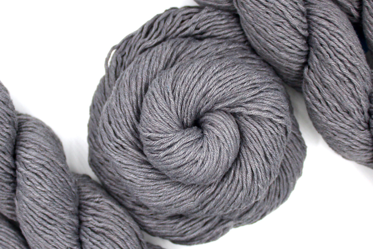 A skein of Vegan, medium Grey, 60% Cotton, 40% Acrylic, DK Weight Yarn recycled by hand from unwanted sweaters swirled attractively in the center of the frame. 