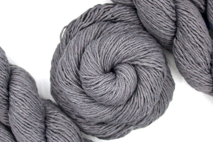 A skein of Vegan, medium Grey, 60% Cotton, 40% Acrylic, DK Weight Yarn recycled by hand from unwanted sweaters swirled attractively in the center of the frame. 