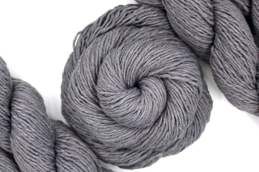 A skein of Vegan, medium Grey, 60% Cotton, 40% Acrylic, DK Weight Yarn recycled by hand from unwanted sweaters swirled attractively in the center of the frame. 
