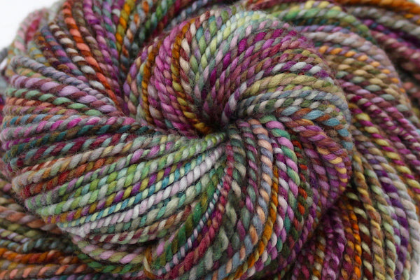 A close up view of a one of a kind, hand dyed variegated skein of multicolored Pink, Orange, Gold, Blue, Green, and Purple self-striping wool Yarn. 