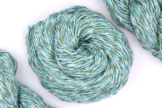 A skein of Light Blue and Green Variegated, Cotton/Acrylic, Dk weight Yarn recycled by hand from unwanted sweaters swirled attractively in the center of the frame. 