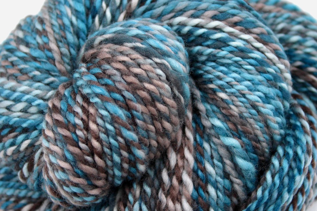 A close up view of a one of a kind, Worsted Weight, hand dyed variegated skein of multicolored Blue, Teal, Taupe, and Chocolate Brown self-striping wool Yarn. 