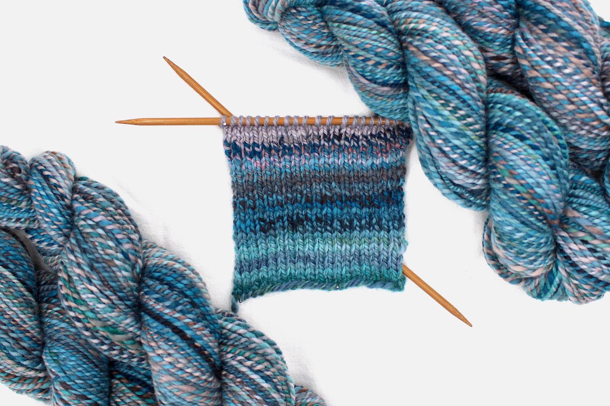 A sample swatch knitted on size 5 knitting needles from a one of a kind, Dk Weight, hand dyed variegated skein of multicolored Blue, Teal, Brown, and Taupe self-striping Hand Spun Yarn, made of 100% Hand Dyed Merino Wool. 