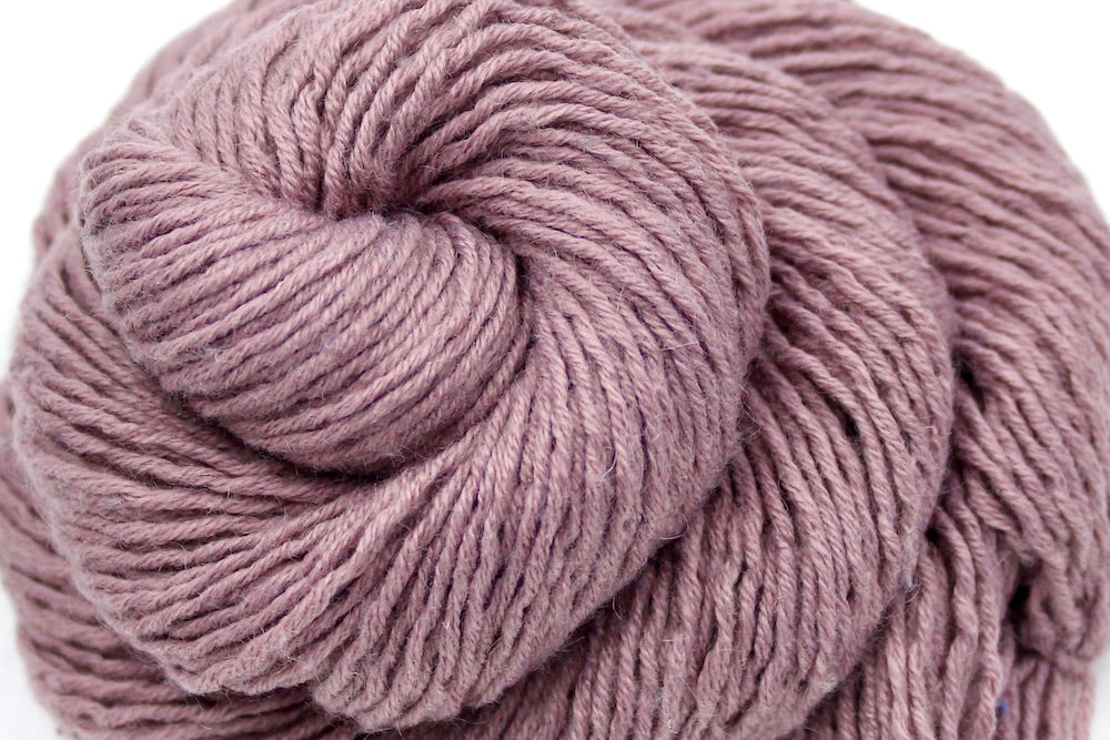 A close up shot of a skein of Dusky Mauve, Acrylic, Nylon, Wool, Mohair, Dk weight Yarn recycled by hand from unwanted sweaters beautifully coiled in the center of the frame. 