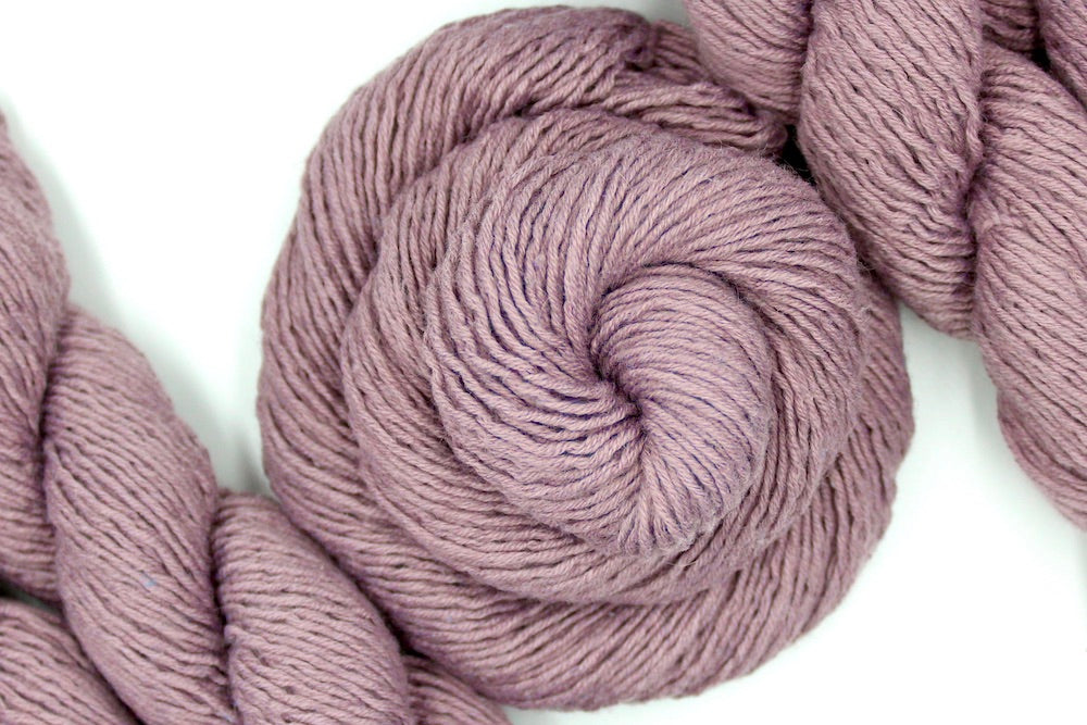 A skein of Dusky Mauve, Acrylic, Nylon, Wool, Mohair, Dk weight Yarn recycled by hand from unwanted sweaters swirled attractively in the center of the frame. 