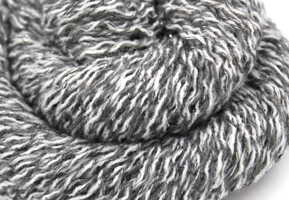 A close up shot of a skein of Vegan, White and Grey Variegated, Acrylic, Polyester, Sparkle, Sport weight Yarn recycled by hand from unwanted sweaters beautifully coiled in the center of the frame. 