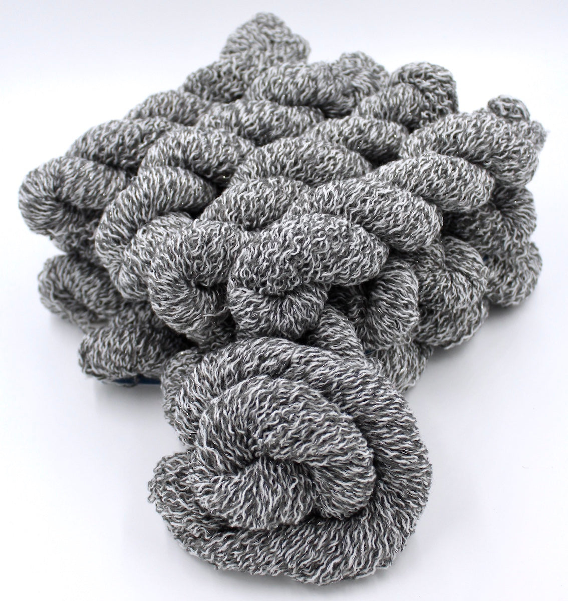 Several skeins of Vegan, White and Grey Variegated, Acrylic, Polyester, Sparkle, Sport weight recycled by hand from unwanted sweaters stacked on top of each other attractively. 