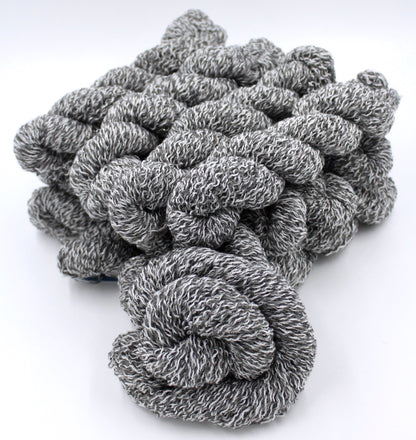 Several skeins of Vegan, White and Grey Variegated, Acrylic, Polyester, Sparkle, Sport weight recycled by hand from unwanted sweaters stacked on top of each other attractively. 