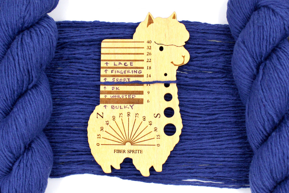 A skein of Vegan, Purplish Blue, Cotton, Nylon, Rayon, Dk Weight Yarn recycled by hand from unwanted sweaters draped over the center of the frame with one strand on top of a Llama shaped Yarn weight tool, to better illustrate the thickness of the yarn. 