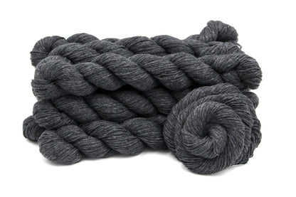 Several skeins of Vegan, Dark Grey, Acrylic/ Cotton, Dk weight recycled by hand from unwanted sweaters stacked on top of each other attractively. 