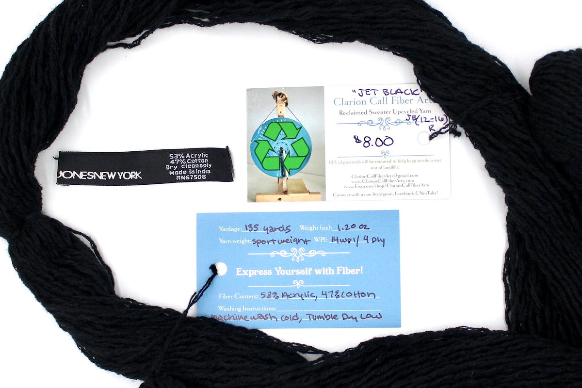 A skein of Vegan, Black, Cotton/ Acrylic, Sport Weight yarn encircling the sweater labels it was recycled from, as well as the hand written yarn tags detailing the specs of this upcycled yarn to help you make your next project! 