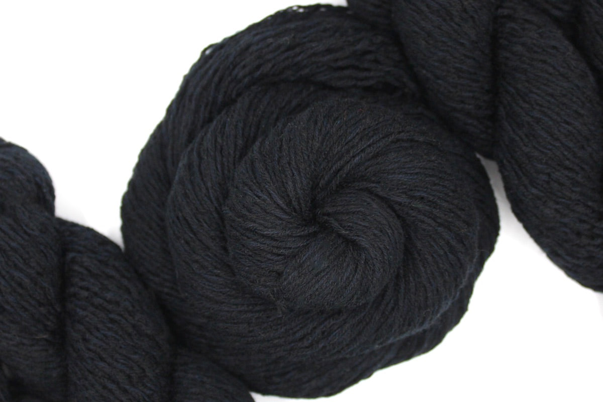 A skein of Vegan, Black, Cotton/ Acrylic, Sport weight Yarn recycled by hand from unwanted sweaters swirled attractively in the center of the frame. 