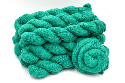 Several skeins of Vegan, Vegan, Jungle Green, Cotton/ Acrylic, Fingering weight recycled by hand from unwanted sweaters stacked on top of each other attractively. 