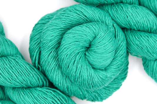 A skein of Vegan, Jungle Green, Cotton/ Acrylic, Fingering weight Yarn recycled by hand from unwanted sweaters swirled attractively in the center of the frame. 