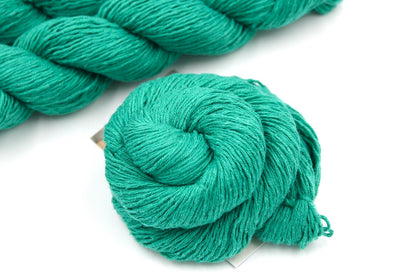 A skein of Vegan, Jungle Green, Cotton/ Acrylic, Fingering weight Yarn recycled by hand from unwanted sweaters swirled attractively in the center of the frame. 